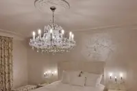 Krištáľový luster Marie Terézie v striebornom prevedení nad posteľou v luxusnej spálni s nástennými svietidlami